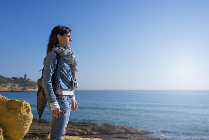 Woman standing tall looking out to the ocean on clear day
