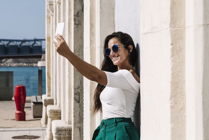 young female in trendy outfit posing for selfie while standing on bright background