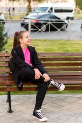 Girl sitting casually on bench and looking around.