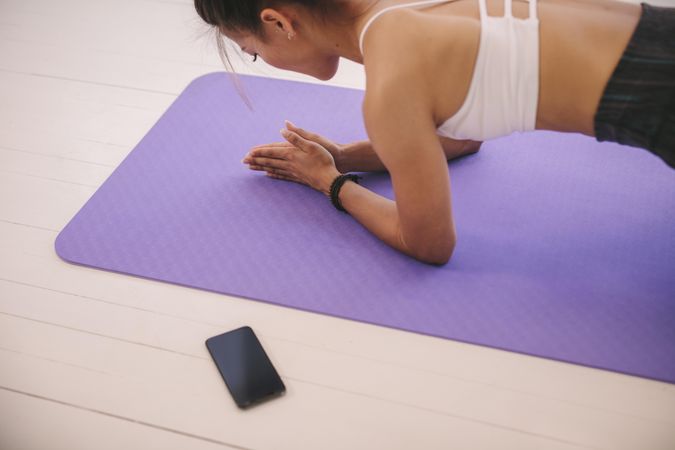 Female holding plank pose in fitness studio with smart phone nearby