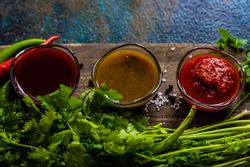 Top view of three traditional Georgian condiments tomato satsebeli, yellow and red tkemali with ingredients on cutting board