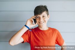 Smiling teenager in red t-shirt standing against wall while using phone 5kRQqP