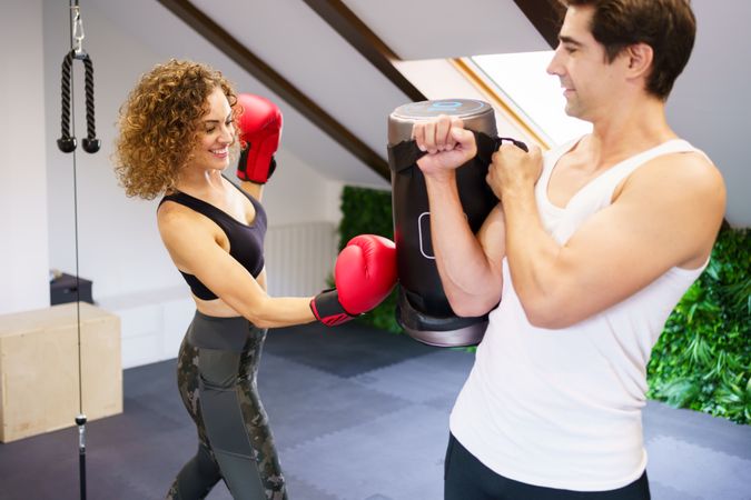 Woman punching punching bag with male trainer