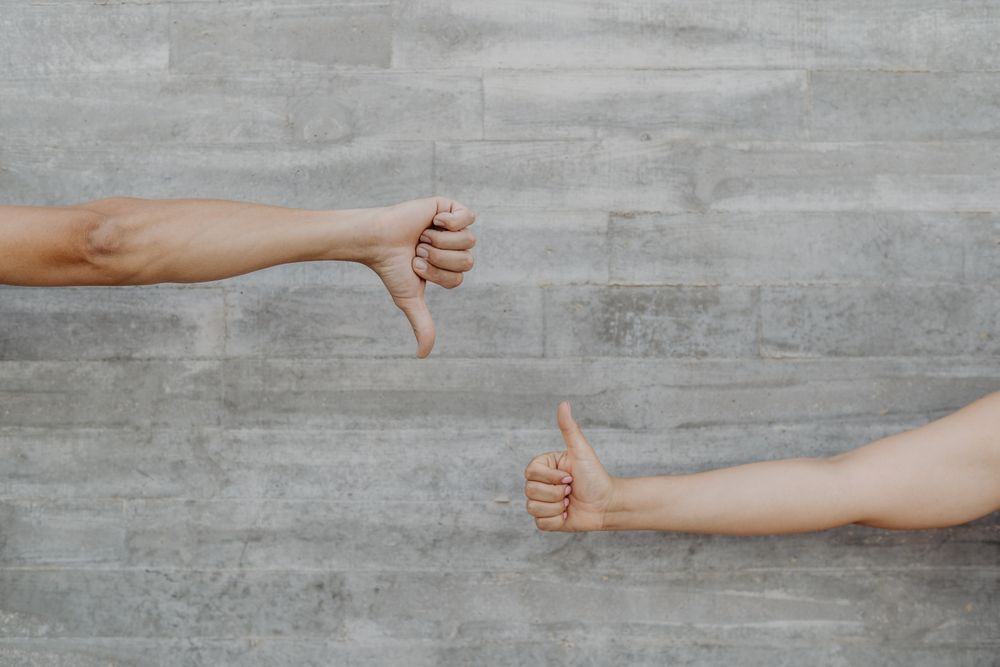 Hands raising thumb up and down on background of grey wall