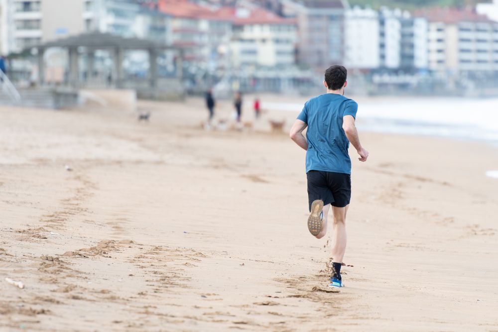 Sportsman in active wear jogging on lonely beach