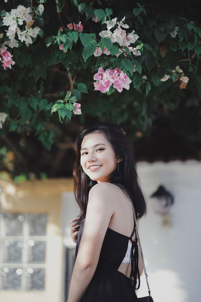 Side view of woman in dark dress standing under floral tree