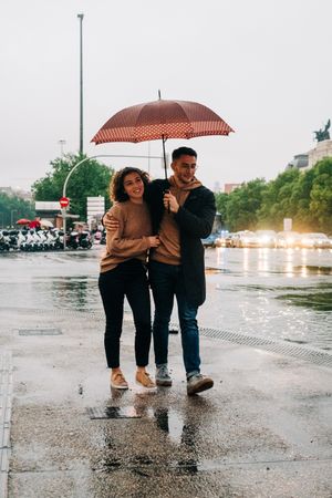 Happy couple with umbrella hugging on wet street