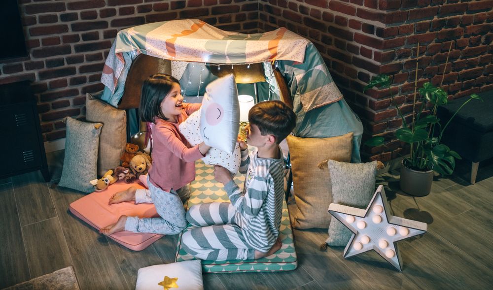 Happy siblings having fun in pillow fight on party at living room. Domestic family life concept.