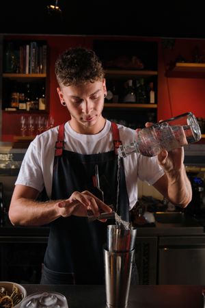 Male barkeeper pouring vodka and syrup into cobbler shaker