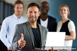 Man with small laptop giving thumbs up in front of his colleagues 56Qql0