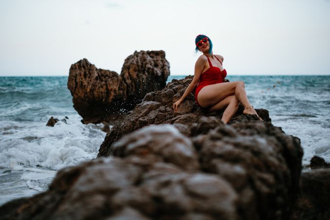 Graceful woman with trendy hairstyle tanning on rocky stone in water