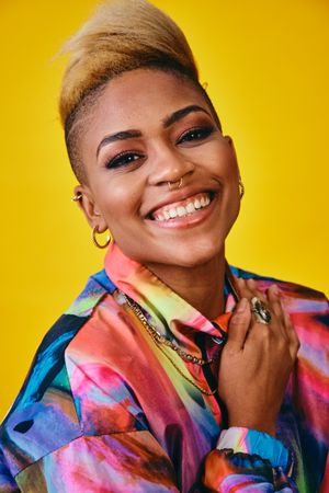 Joyful Black woman in bright 80s windbreaker jacket in yellow studio