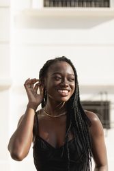 A young Black woman smiles happily as she fixes her hair with her hand