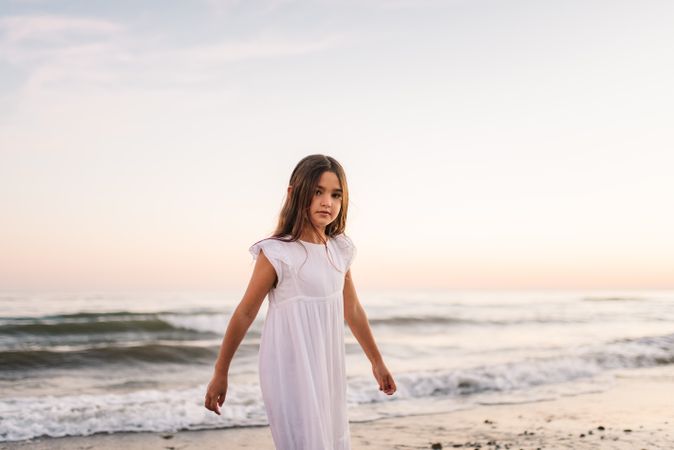 Adorable girl walking and looking at camera on seaside at sunset