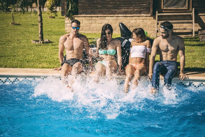 Friends sitting on poolside and splashing with their feet