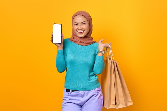 Muslim woman showing phone screen and holding shopping bags
