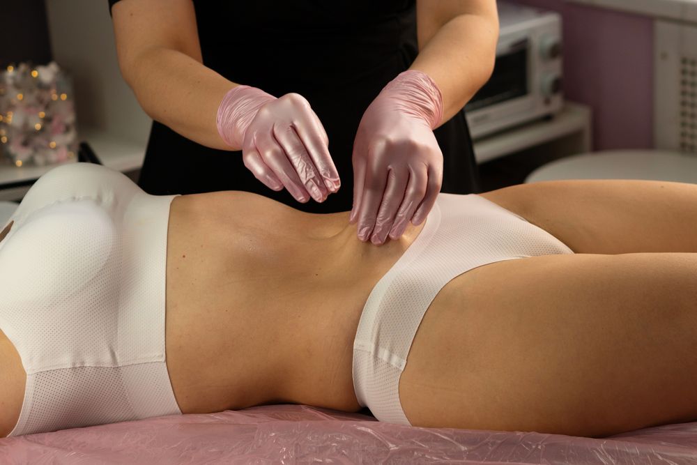 Aesthetician performs abdominal massage wearing pink protective gloves.