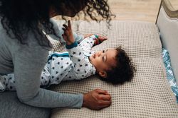 Cute baby boy lying down reaching for his mother’s face