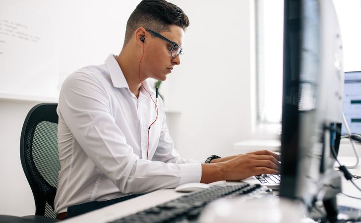 Man wearing spectacles typing on laptop computer in office