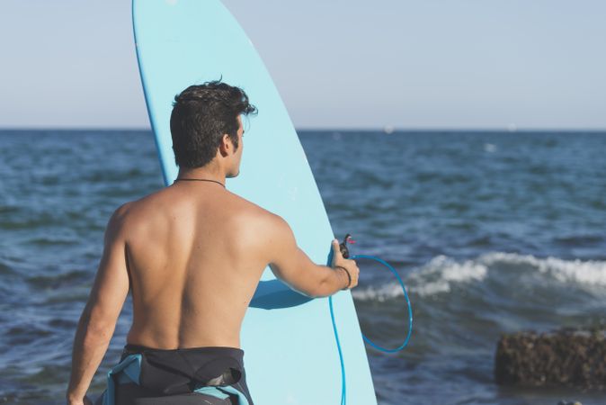 Male surfer holding blue board standing in front of the ocean