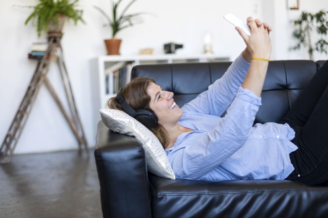 Woman lying on a leather sofa taking selfie on her phone