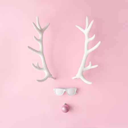 Reindeer face made of sunglasses and pink bauble on pink background