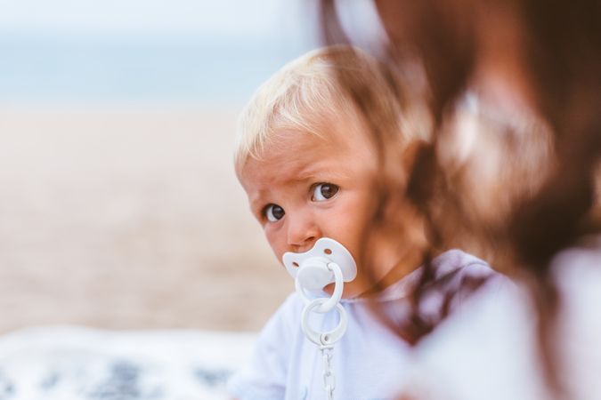 Blond baby with pacifier on the beach