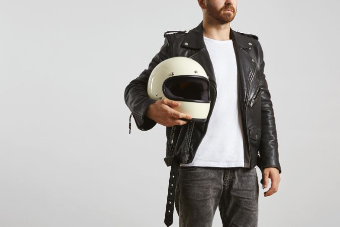 Man in dark leather jacket with light t-shirt holding motorcycle helmet