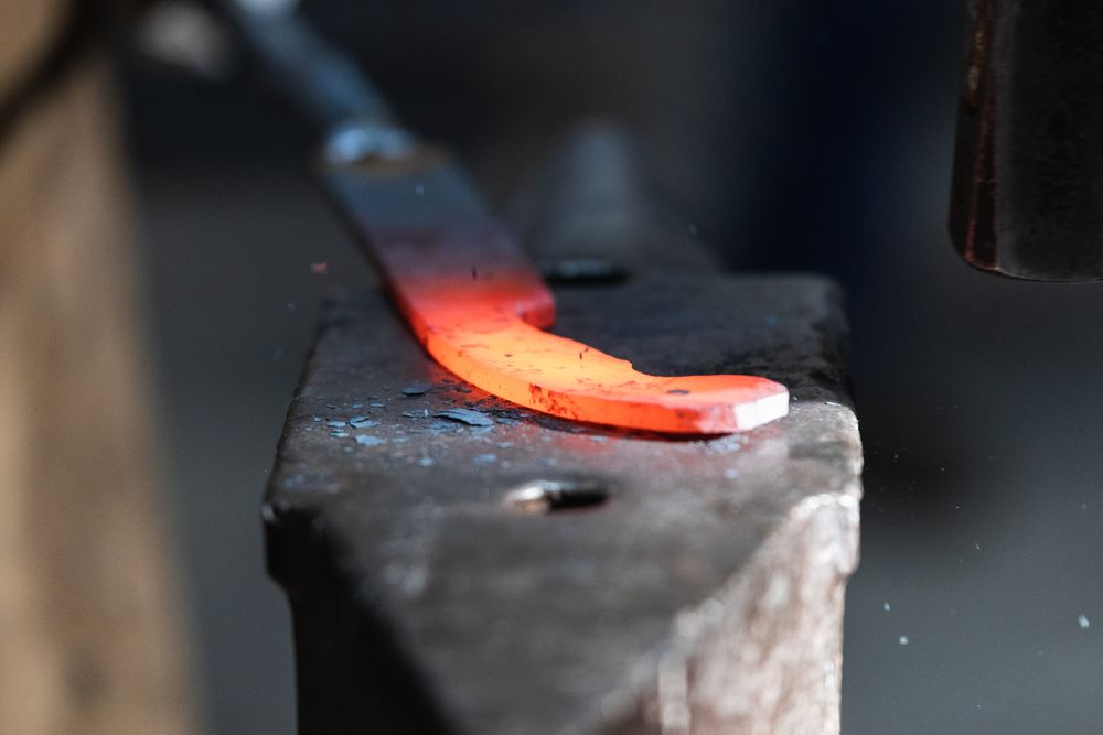 Blacksmiths forging hot metal with hammer in workshop