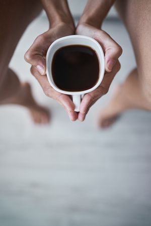 Faceless woman showing ceramic cup with coffee