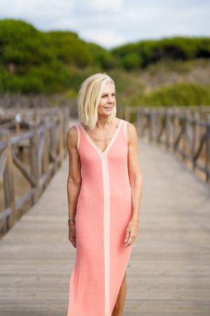 Happy mature woman with grey hair strolling on wooden walkway near the coast, vertical