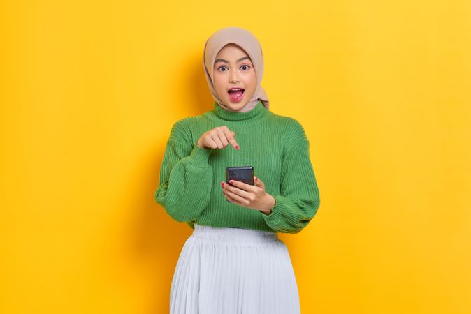 Woman in headscarf smiling and pointing at smart phone