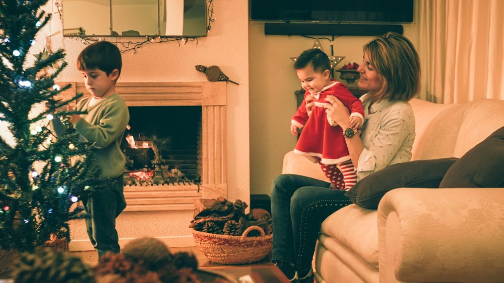 Mother playing with baby while son decorating Christmas tree