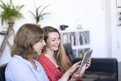 Two happy females at home sitting on sofa using digital tablet