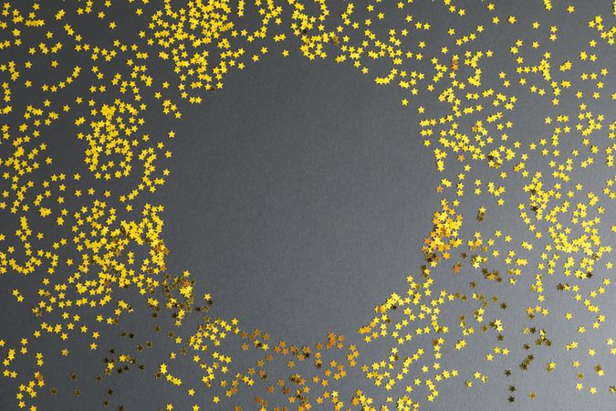 Gold glitter stars circle on dark background, space for text