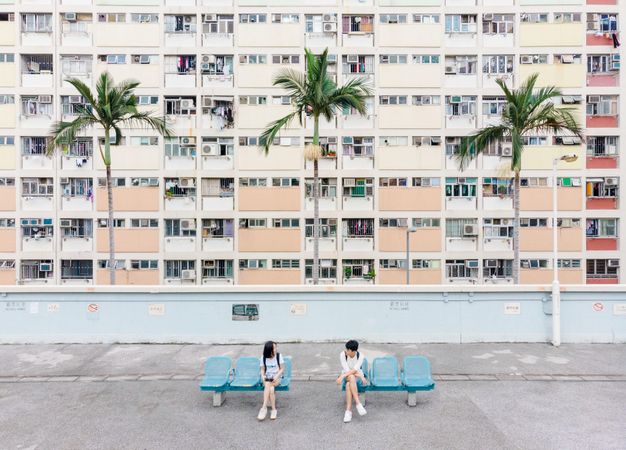 Two girls sitting on outdoor concrete bench beside a building