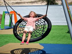 Curly shining preteen boy playing on nest swing