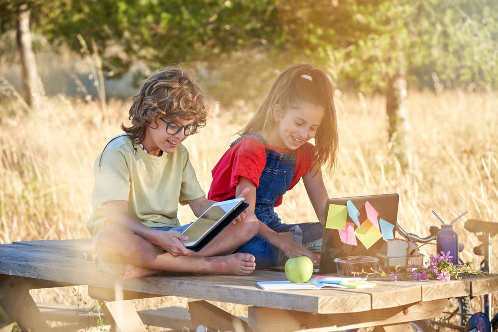 Children laughing while browsing tablet and laptop in nature