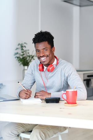 Cheerful Black economist with notebook and headphones at home