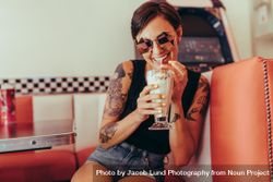 Woman with tattooed arms drinking milkshake sitting at a restaurant 0ynrW5