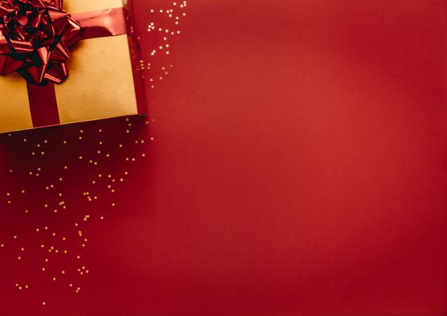 Flat lay of golden colored gift box with star confetti on red background