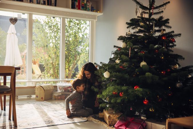 Mother and son sitting by Christmas tree at home