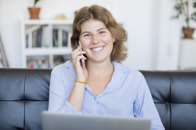 Female entrepreneur sitting on sofa at home using a laptop and speaking on phone