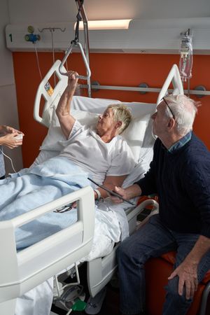 Older female patient lying near husband and talking to crop doc