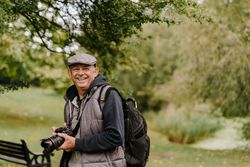 Older man smiling with large camera in a park 4Aev64
