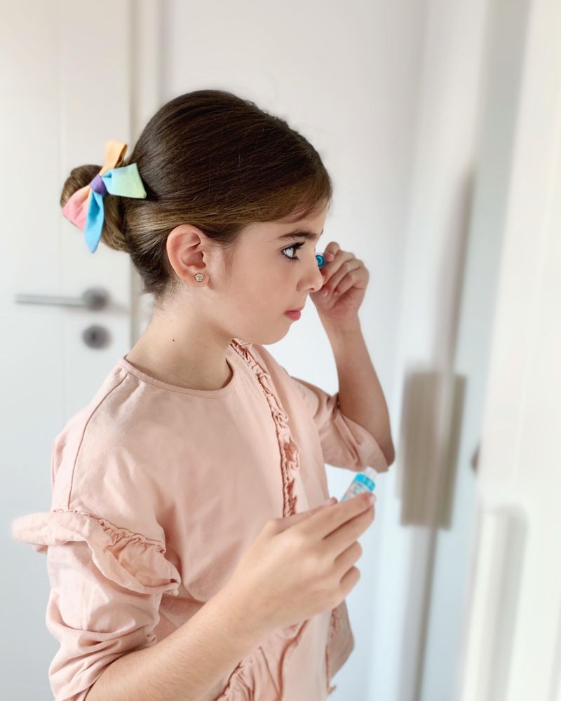 Young girl standing in front of the mirror applying mascara