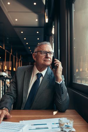 Businessman sitting relaxed at cafe making a phone call and looking outside the window