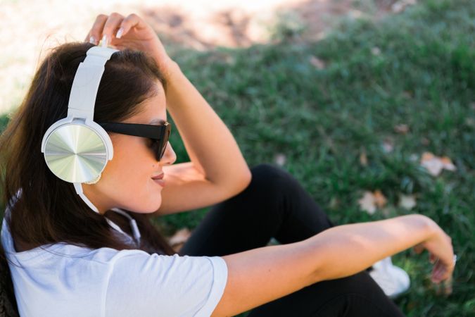 Relaxed trendy woman in headphones resting in park on grass
