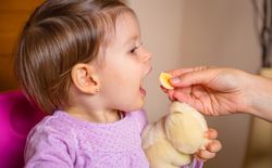 Baby eating banana slice from the hand of mother