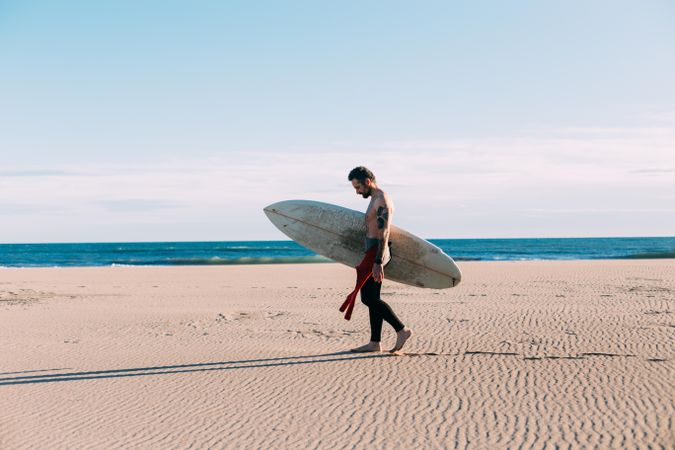 Man in wetsuit walking along the coast with surfboard